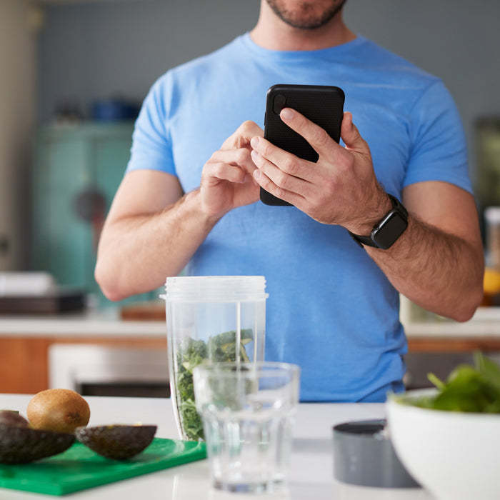 Close Up Of Man Using Fitness Tracker To Count Calories For Post Workout Juice Drink He Is Making