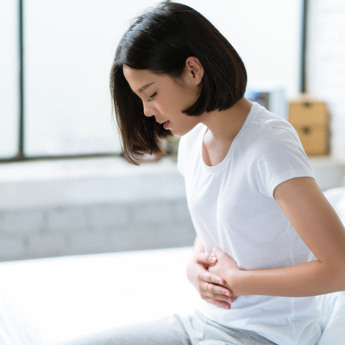 Woman with a stomach ache places hands on stomach in bed